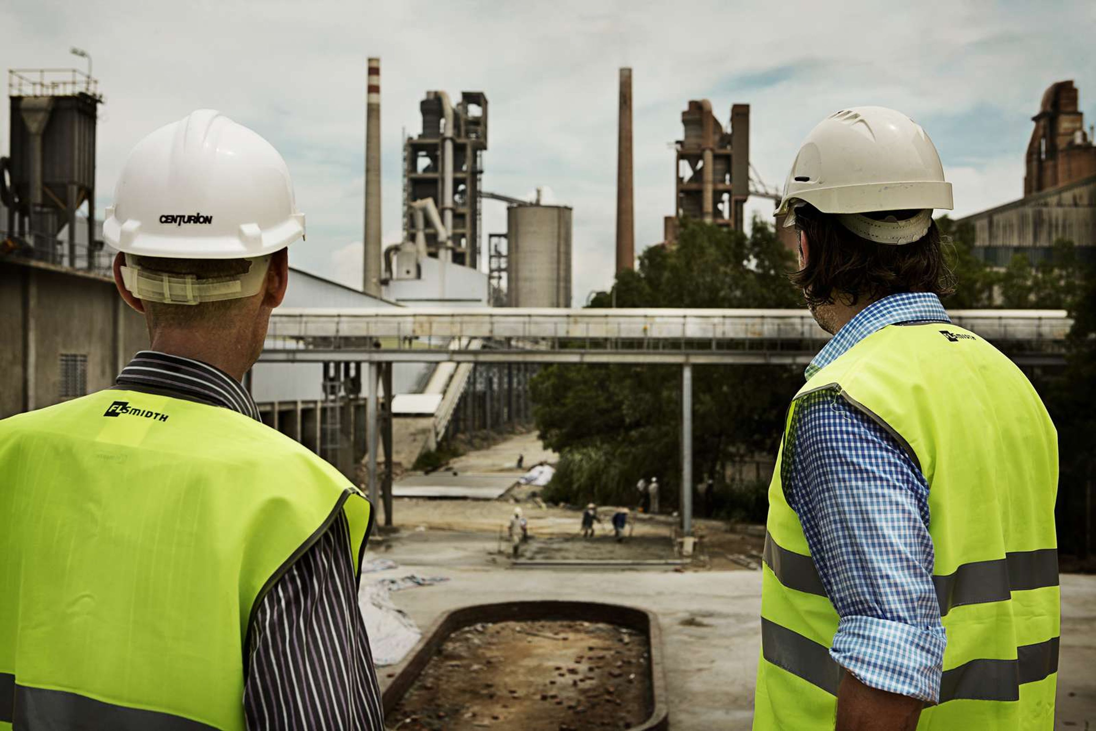 Construction workers observing cement plant operations from a distance